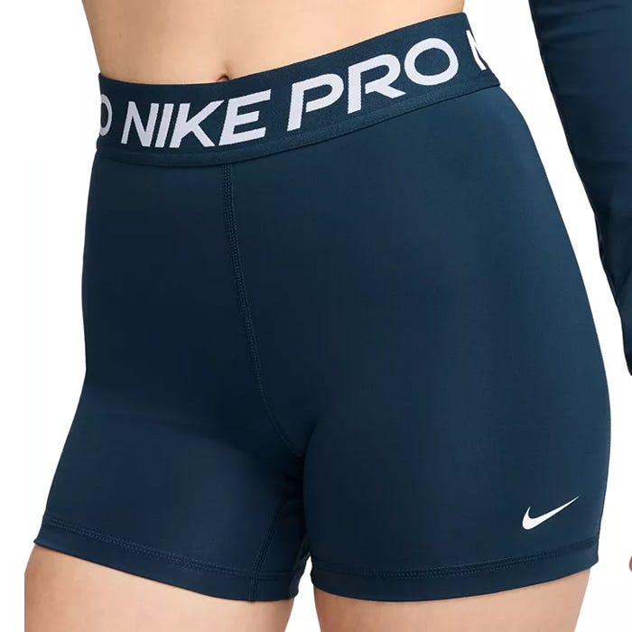 Navy blue women's athletic shorts with a 5-inch inseam, featuring a wide waistband with \“NIKE PRO\“ in bold letters and a small Nike Swoosh logo near the hem.