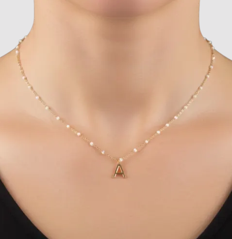 A delicate gold chain necklace with small pearls features a prominent capital letter \“A\“ pendant at the center.