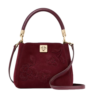 A burgundy handbag with floral embroidery, gold accents, and a top handle. It features a turn-lock closure and an adjustable shoulder strap.