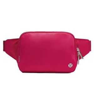 A pink waist bag with a zippered front pocket, featuring a small logo and adjustable strap, ideal for carrying essentials.