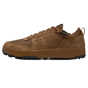 A brown Nike sneaker with suede panels and a textured fabric upper, featuring the Nike logo on the side and a label indicating Cordura fabric. It has a rugged, dark sole and a pull tab at the heel.