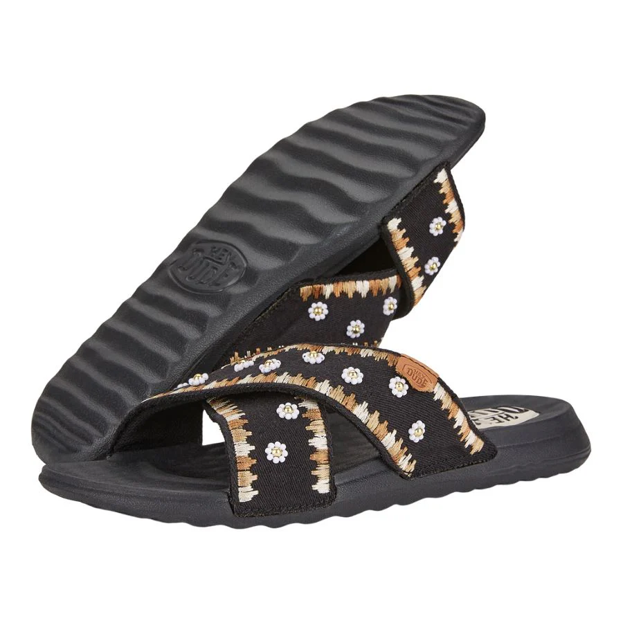 Sandal with adjustable black straps featuring a white and brown floral pattern and a ridged black sole.