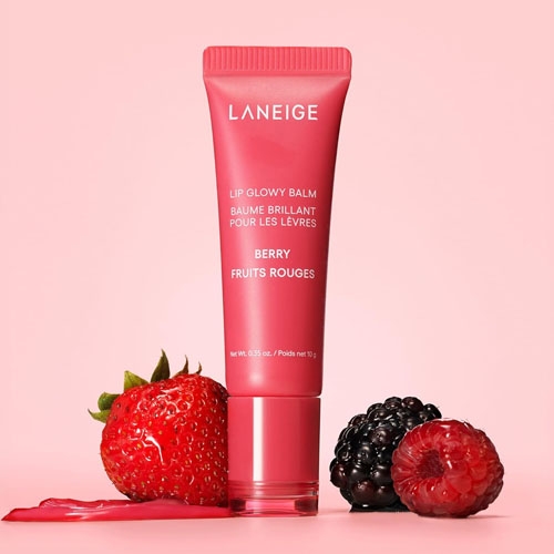 a tube of lip balm besides berries on a pink background
