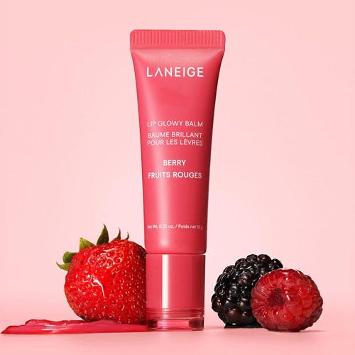 a tube of lip balm besides berries on a pink background