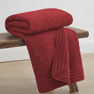 A red quilt with a textured, quilted pattern is draped over a wooden bench.