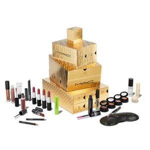 24-piece MAC Advent Calendar features gold stacked boxes with numbered compartments, containing a variety of lipsticks, lip glosses, eyeshadows, mascaras, eyeliners, face masks, and nail polishes in assorted colors and finishes.