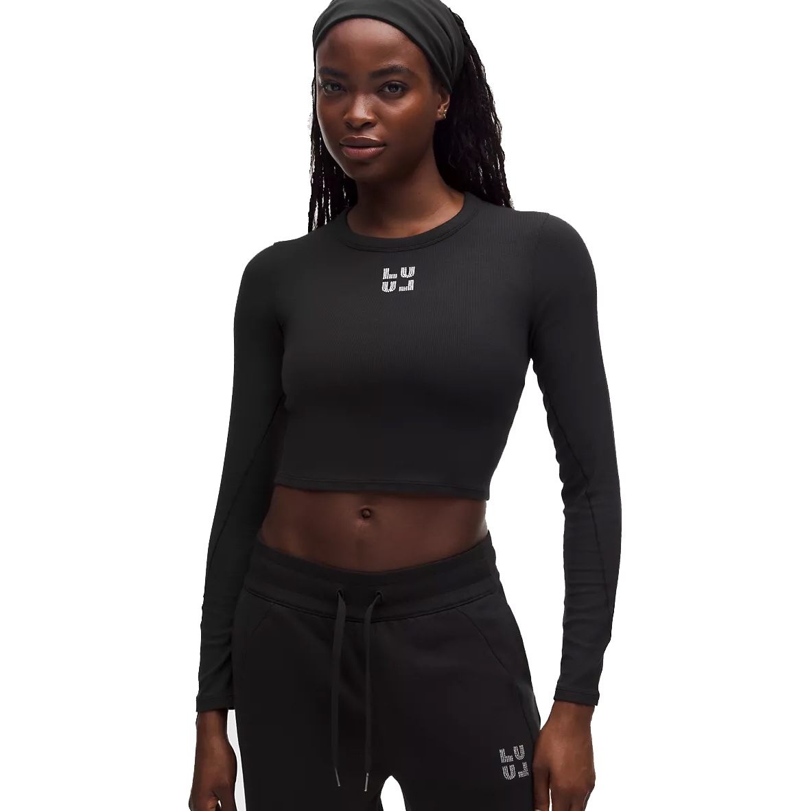 A woman wearing a black long-sleeve crop top and black sweatpants, both with a small \“LUJ\“ logo.