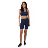 A woman is wearing a matching navy sports bra and high-waisted biker shorts, paired with dark sneakers.