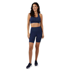 A woman is wearing a matching navy sports bra and high-waisted biker shorts, paired with dark sneakers.