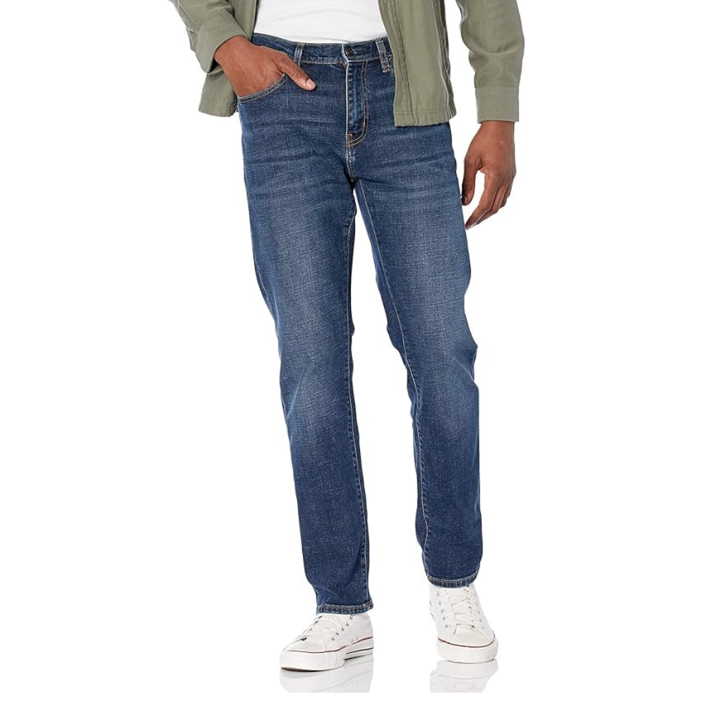 A person is wearing blue jeans with a slight fade, an olive green jacket, and white sneakers.