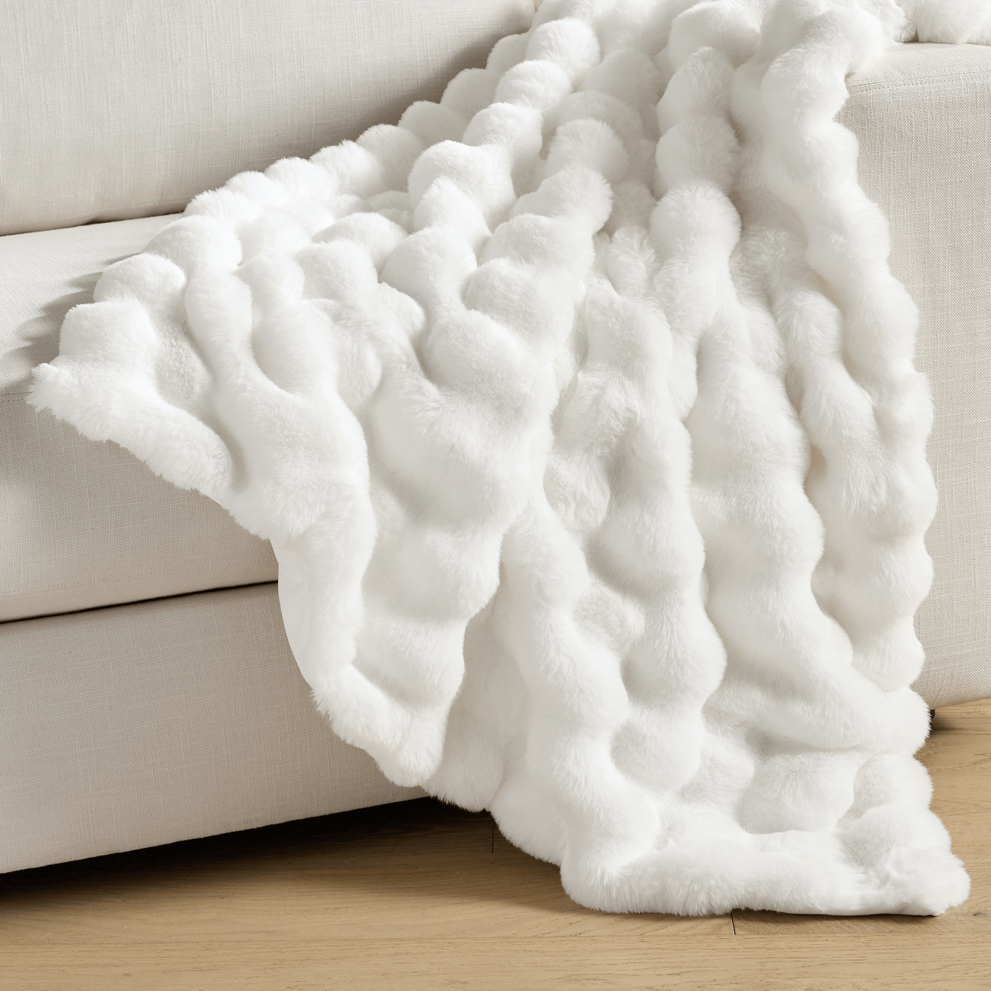 A white, textured faux fur throw blanket is draped over a light-colored sofa, showcasing a cozy and luxurious design.