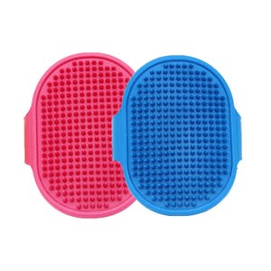 Two oval-shaped, rubber grooming brushes with short bristles, one pink and one blue, featuring handles on the sides.