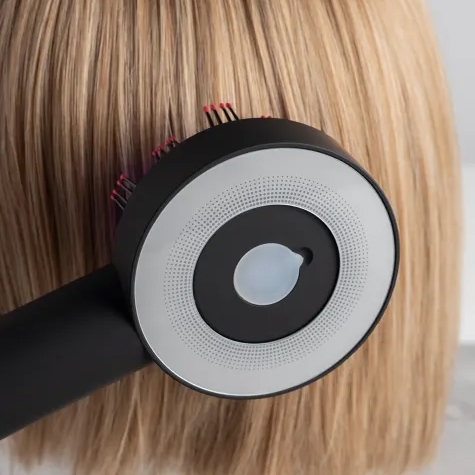 A hairdryer with a circular design is shown drying or styling blonde hair.