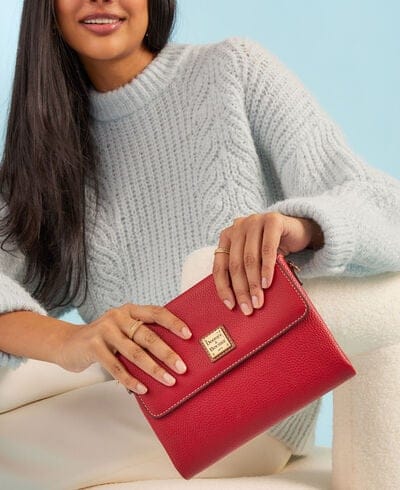A person in a light blue sweater holds a red textured handbag with a gold-toned clasp.