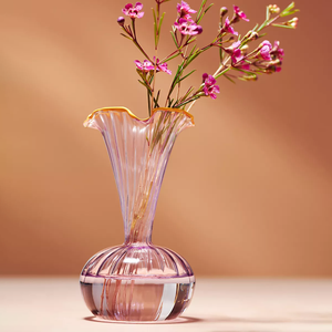 A translucent pink glass vase with an elegant flared rim and ribbed detailing holds a spray of pink flowers.