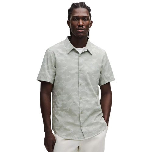 A man wears a short-sleeve, button-up shirt with a light camo pattern, paired with white pants.