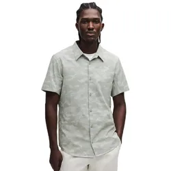 A man wears a short-sleeve, button-up shirt with a light camo pattern, paired with white pants.