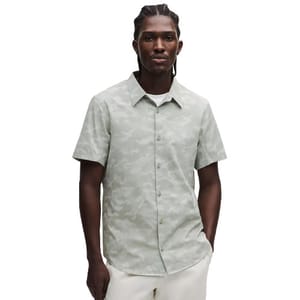 A man wears a short-sleeve, button-up shirt with a light camo pattern, paired with white pants.