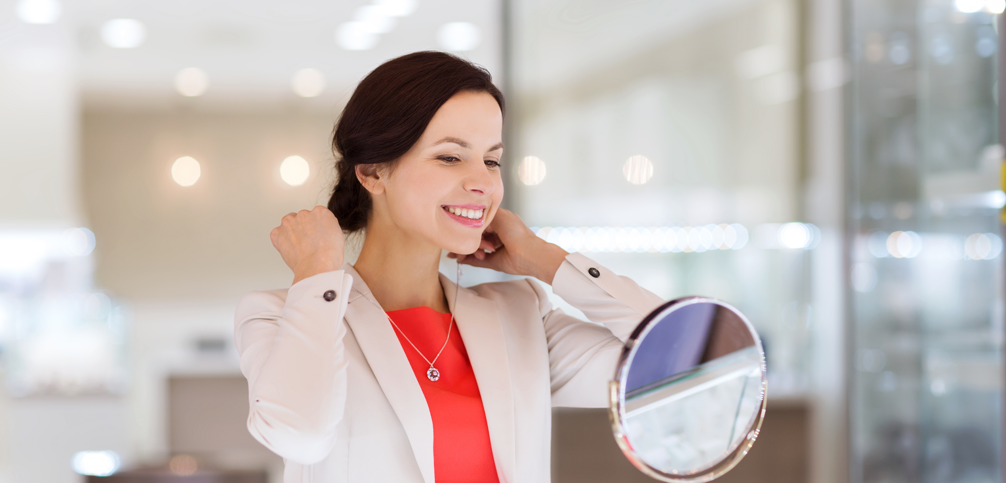 A woman is trying on a pendant necklace and holding matching earrings.