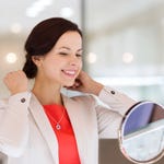 A woman is trying on a pendant necklace and holding matching earrings.
