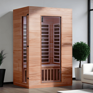 A wooden infrared sauna with a glass door, placed indoors next to a white couch and green plants.