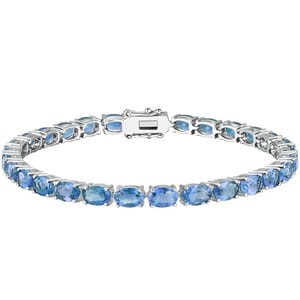A tennis bracelet featuring a single row of oval-cut blue stones set in a silver-toned metal with a secure clasp.