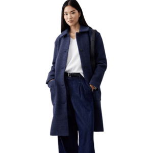 Woman wearing a navy blue textured coat, white top, wide-leg denim trousers, black belt, and black shoes, carrying a black shoulder bag.