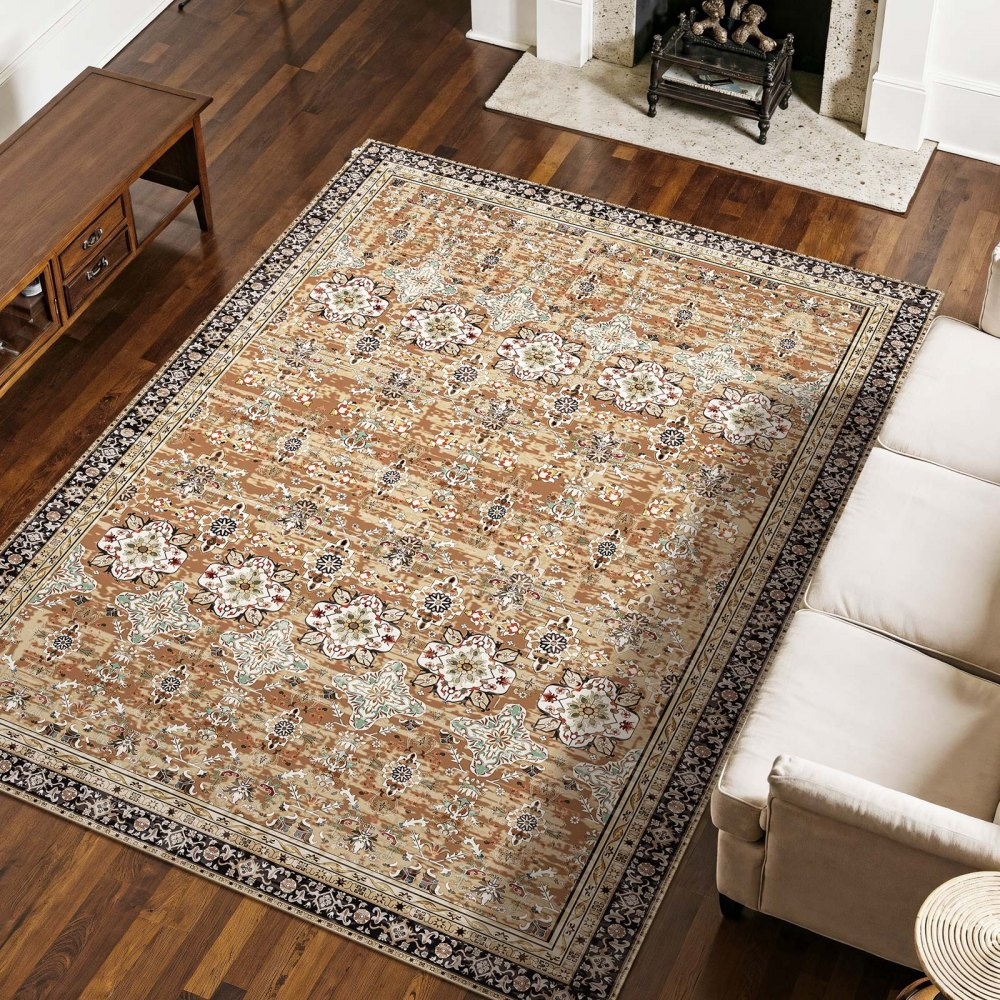 A large patterned rug with earthy tones is placed on a hardwood floor, partially under a beige sofa. It features floral designs and intricate borders, adding an elegant touch to the living room setting.