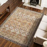 A large patterned rug with earthy tones is placed on a hardwood floor, partially under a beige sofa. It features floral designs and intricate borders, adding an elegant touch to the living room setting.