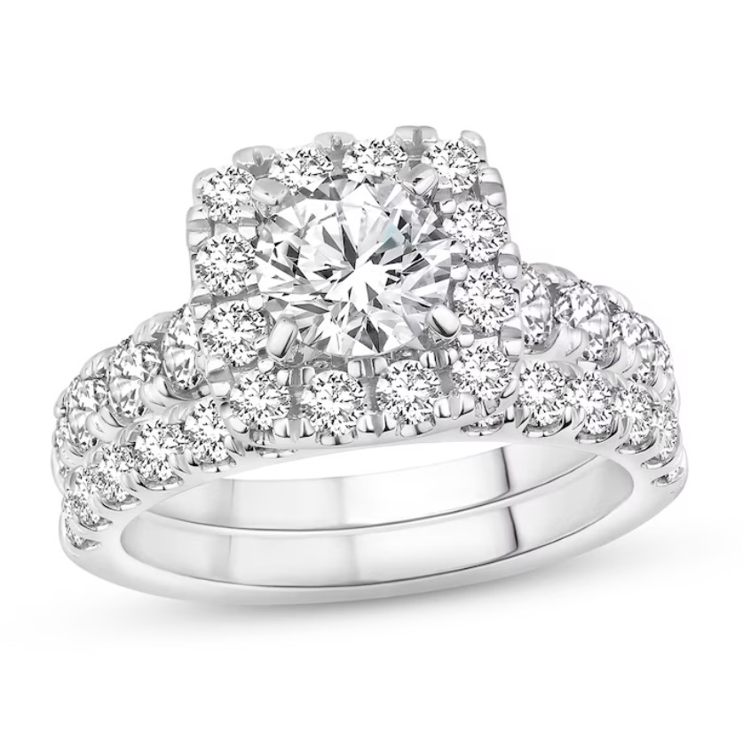 A stunning bridal set featuring a large round center diamond, surrounded by a halo of smaller diamonds. The set includes two bands adorned with diamonds, creating a sparkling and elegant design in a white metal setting.