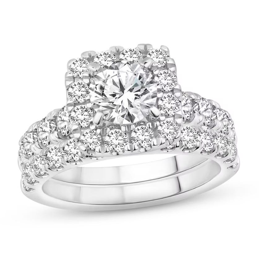 A stunning bridal set featuring a large round center diamond, surrounded by a halo of smaller diamonds. The set includes two bands adorned with diamonds, creating a sparkling and elegant design in a white metal setting.