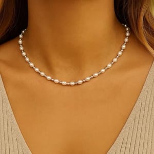 A woman wearing a delicate pearl necklace with evenly spaced small pearls, complementing a beige ribbed-textured top.