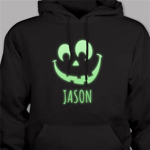 Black hoodie with a glowing green jack-o'-lantern design and the name \“JASON\“ below it.