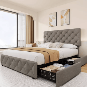 The photo shows a modern upholstered bed with a tufted headboard and footboard, featuring built-in storage drawers underneath. It's set in a bright bedroom with a large window and simple wall art.