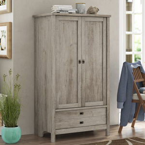 A wooden wardrobe with two doors and two drawers in a light, rustic finish stands next to a window. A potted plant and chair with a blue jacket are nearby, with books stacked on the wardrobe and chair.