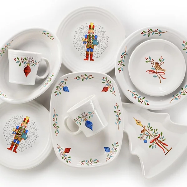 A collection of holiday-themed dinnerware featuring plates, mugs, and a tree-shaped dish, adorned with colorful designs of nutcrackers, birds, and festive ornaments.