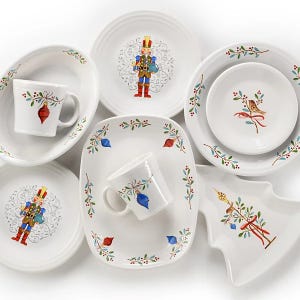 A collection of holiday-themed dinnerware featuring plates, mugs, and a tree-shaped dish, adorned with colorful designs of nutcrackers, birds, and festive ornaments.