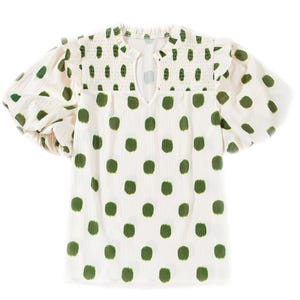 White polka dot top with smocked detailing around the neckline and shoulders, featuring green oval-shaped dots and puffed sleeves.