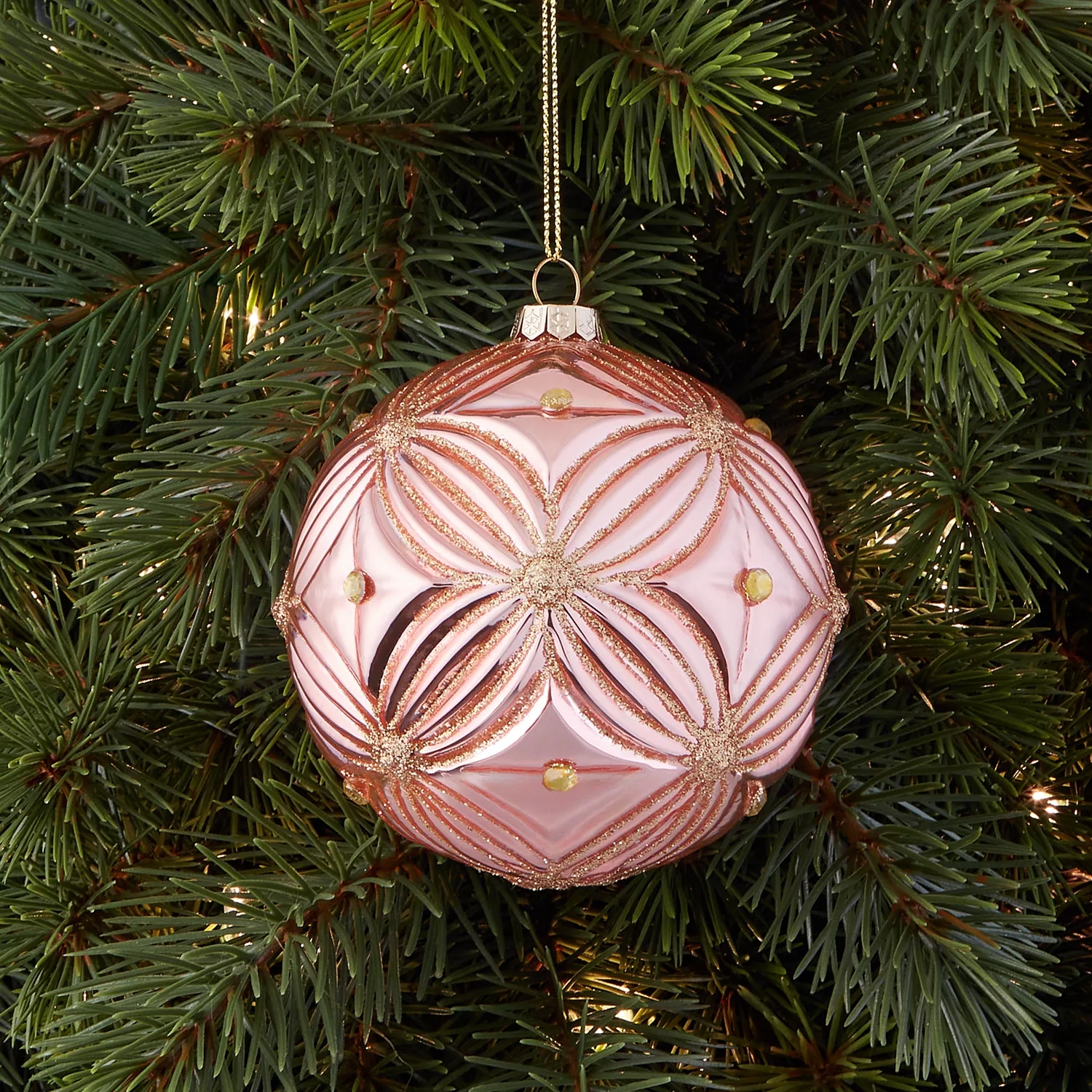 Pink Christmas ornament with gold glitter patterns and small gemstones, hanging on a green Christmas tree.