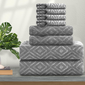 A stack of grey towels with a diamond pattern, neatly arranged from large to small, accompanied by a plant for a decorative touch.