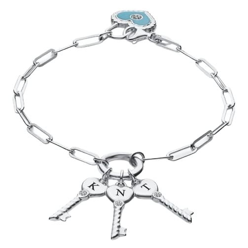 A silver bracelet features a paperclip chain with three key charms, each engraved with a letter (K, N, T). It also includes a turquoise heart charm with a sparkling accent.