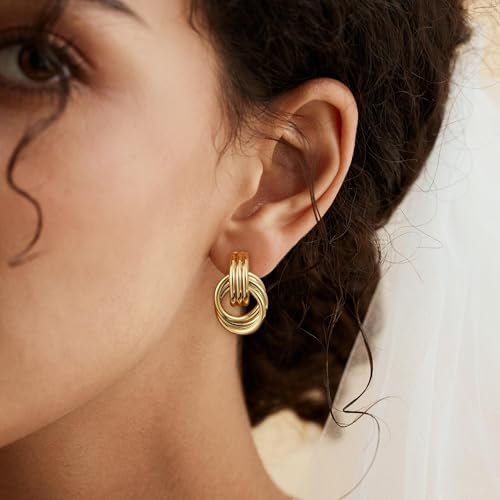 Gold knot earrings worn by a person with curly hair. The earrings have a multi-looped design.