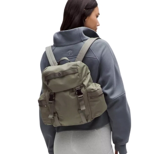 A woman is wearing a green lululemon Wanderlust Mini Backpack. The bag features multiple pockets, adjustable straps, and buckle closures.