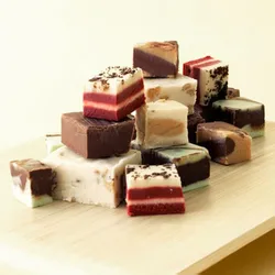 A 1lb assortment of Boscov’s Fudge features a variety of square pieces with layers of different colors and flavors, including chocolate, vanilla, and possibly red velvet, all presented on a wooden surface.