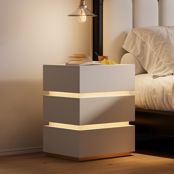 A modern nightstand with a tiered, floating design features integrated LED lighting between each segment, placed beside a bed with neutral bedding. A book and a small bunch of grapes rest on top.