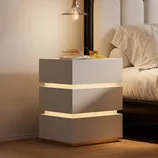 A modern nightstand with a tiered, floating design features integrated LED lighting between each segment, placed beside a bed with neutral bedding. A book and a small bunch of grapes rest on top.