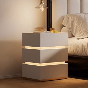 A modern nightstand with a tiered, floating design features integrated LED lighting between each segment, placed beside a bed with neutral bedding. A book and a small bunch of grapes rest on top.