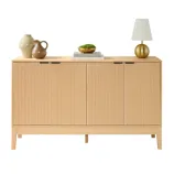 A light wood sideboard with vertical grooves features two pottery vases, two stacked books, a bowl with greenery, and a gold lamp on top.