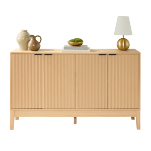 A light wood sideboard with vertical grooves features two pottery vases, two stacked books, a bowl with greenery, and a gold lamp on top.