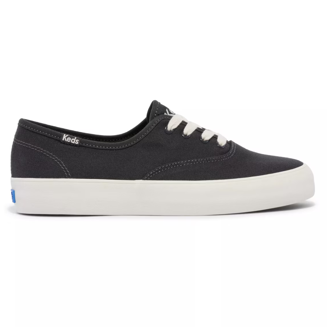 A black canvas sneaker with white laces and a white rubber sole, labeled \“Keds\“ on the side.